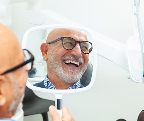Man smiling in reflection of handheld mirror